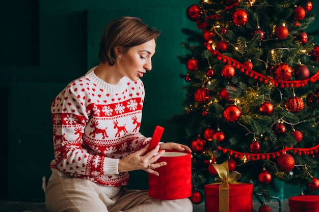 Joven mujer sentada junto al árbol de Navidad con cajas rojas