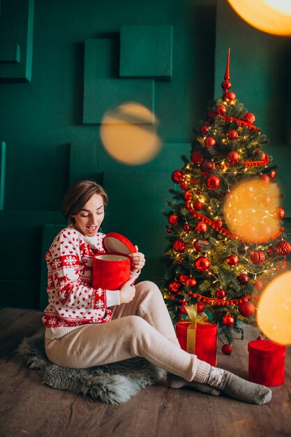 Joven mujer sentada junto al árbol de Navidad con cajas rojas