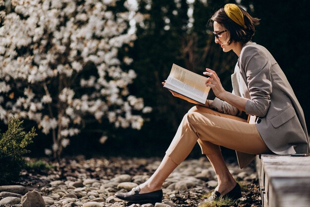 Joven mujer sentada en el patio trasero y leyendo el libro