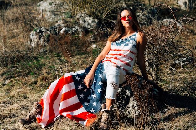 Foto gratuita joven mujer sentada en piedra con bandera