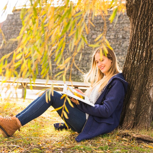 Joven mujer sentada bajo la rama de un árbol y leyendo