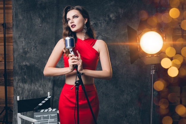 Joven mujer sexy con estilo en el cine entre bastidores, celebrando, vestido de noche de satén rojo