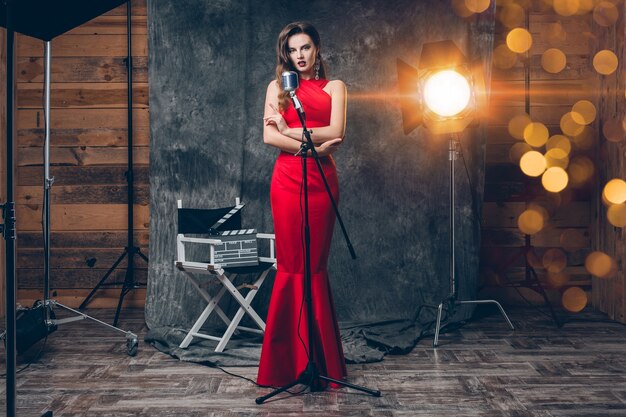 Joven mujer sexy con estilo en el cine entre bastidores, celebrando, vestido de noche de satén rojo