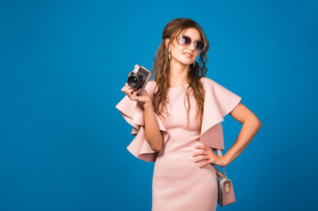 Joven mujer sexy con estilo en vestido rosa de lujo, tendencia de la moda de verano, estilo chic, gafas de sol, tomando fotografías con cámara vintage