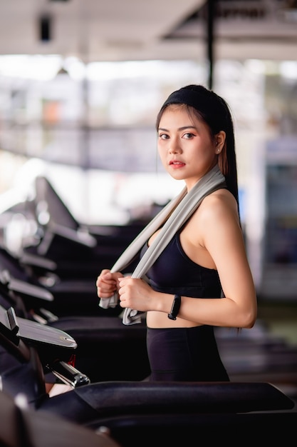 Joven mujer sexy con ropa deportiva, tela a prueba de sudor y reloj inteligente caminando en la cinta de correr calentar antes de correr para entrenar en el gimnasio moderno, espacio de copia