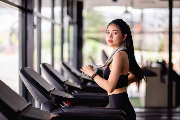 Joven mujer sexy con ropa deportiva, tela a prueba de sudor y reloj inteligente caminando en la cinta de correr calentar antes de correr para entrenar en el gimnasio moderno, espacio de copia