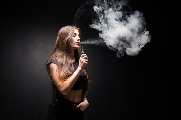 Joven mujer sexy vaping fumar cigarrillo electrónico. nube de vapor en la pared negra
