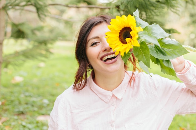 Joven mujer sonriendo y cubriendo el ojo con girasol