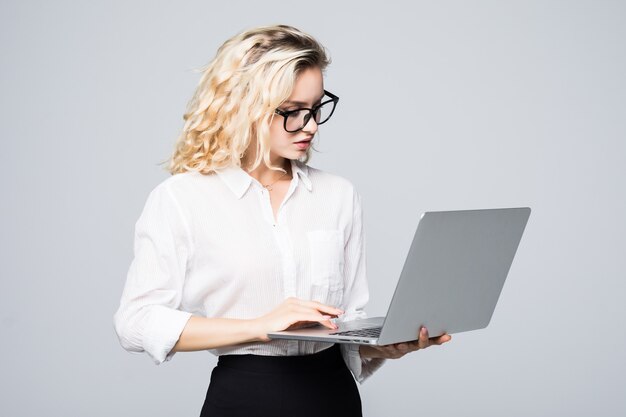 Joven mujer sonriente feliz en ropa casual sosteniendo una computadora portátil y enviando un correo electrónico a su mejor amiga