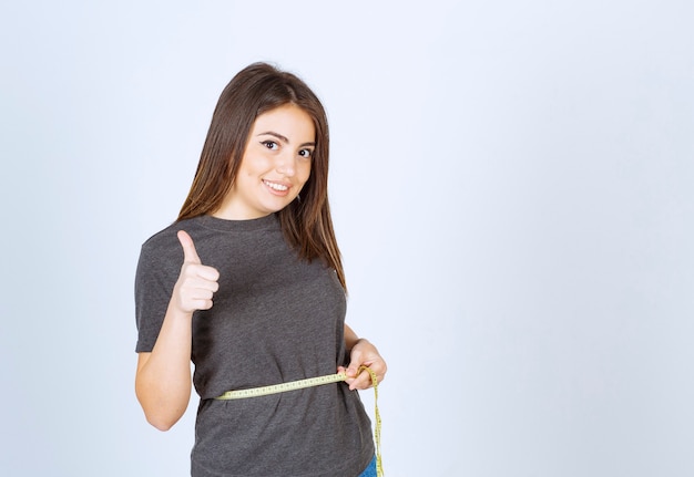 Una joven mujer sonriente midiendo la cintura y mostrando un pulgar hacia arriba.