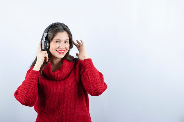 Una joven mujer sonriente en suéter rojo cálido de pie con auriculares