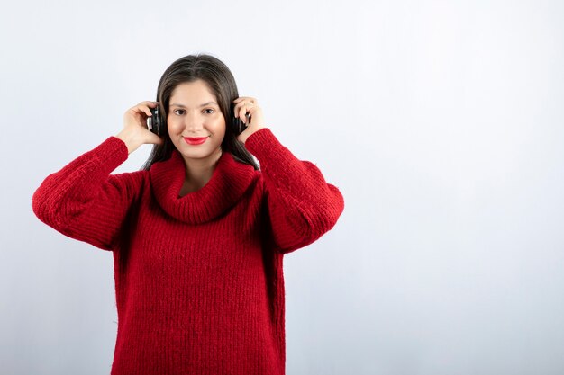 Una joven mujer sonriente en suéter rojo cálido de pie con auriculares