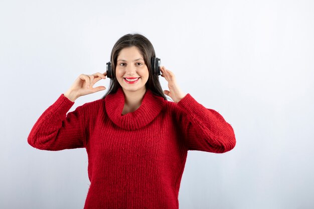 Una joven mujer sonriente en suéter rojo cálido de pie con auriculares