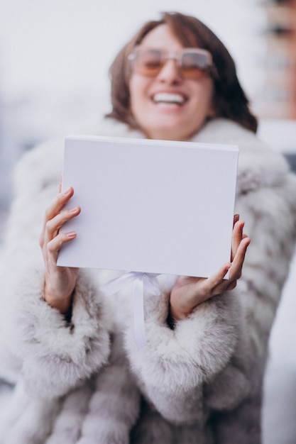 Foto gratuita joven mujer sosteniendo una caja de regalo blanca al aire libre