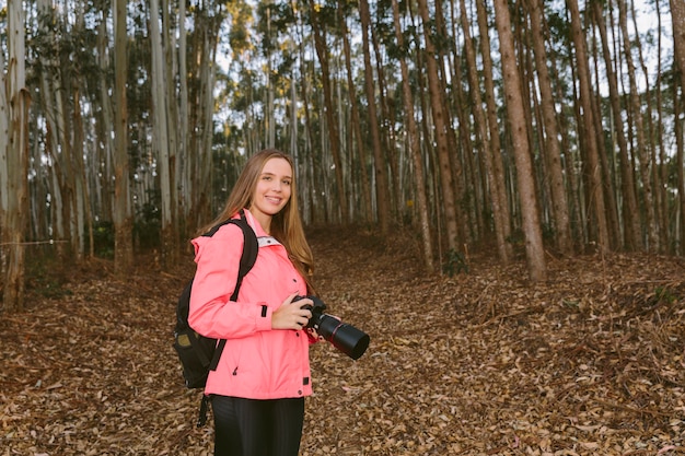 Joven mujer sosteniendo la cámara en el bosque