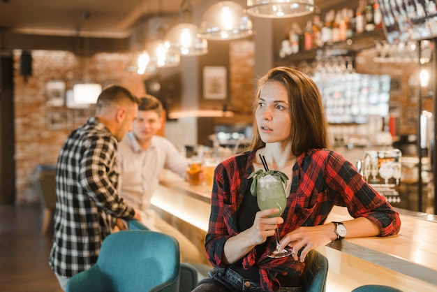Joven mujer sosteniendo una copa de cóctel en la barra