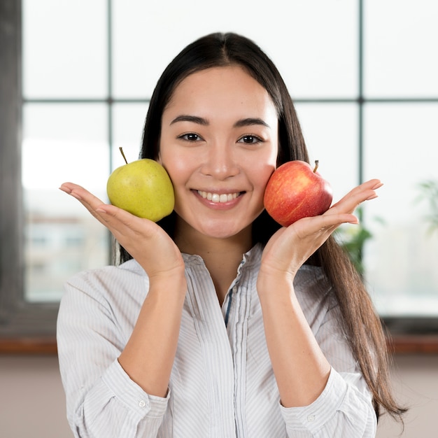 Joven mujer sosteniendo dos manzanas verdes y rojas