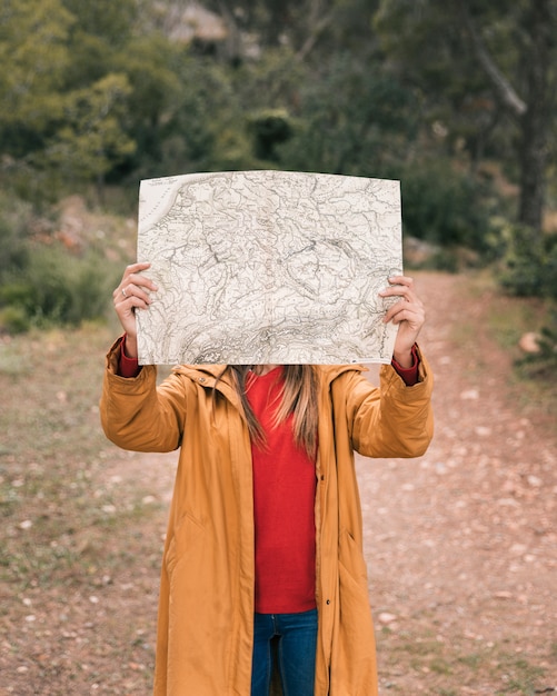 Foto gratuita una joven mujer sosteniendo un mapa delante de su cara