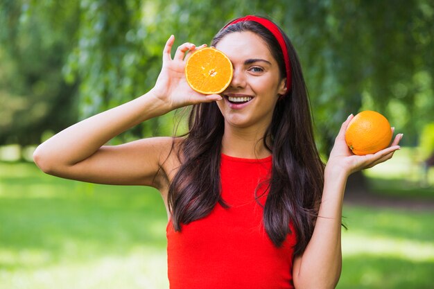 Joven mujer sosteniendo naranja a la mitad frente a su ojo en el parque