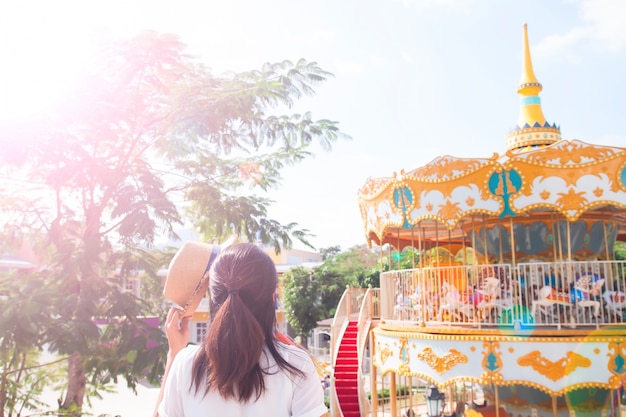 Joven mujer sosteniendo el sombrero en día soleado con fondo de paseo parque de atracciones