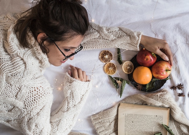 Joven mujer tendida sobre una manta con plato de frutas