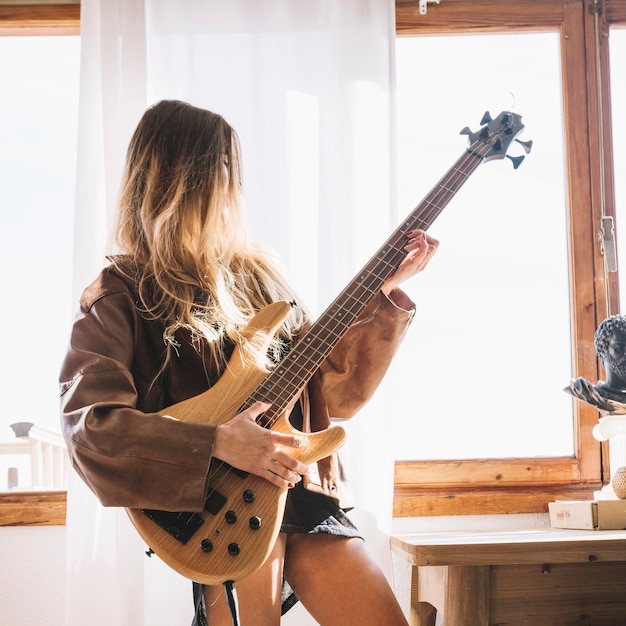 Joven mujer tocando la guitarra junto a la ventana