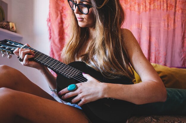 Joven mujer tocando el ukelele en la cama