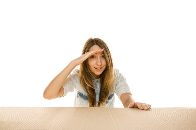 Joven mujer triste abriendo el paquete postal más grande aislado en blanco. Conmocionado modelo femenino molesto en la parte superior de la caja de cartón mirando hacia adentro.