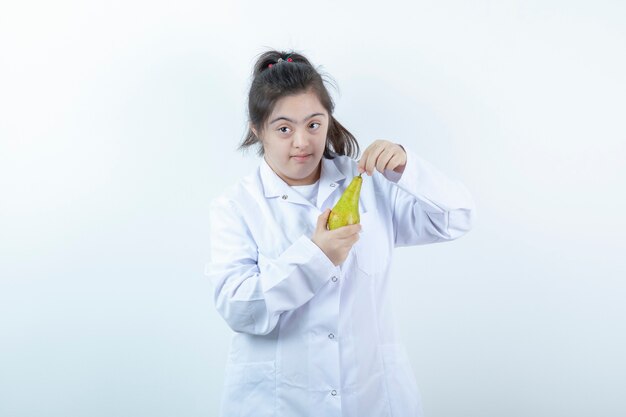 Joven mujer en uniforme de médico con fruta de pera.