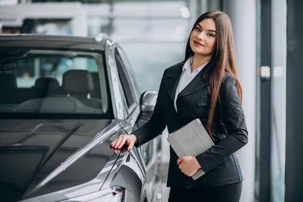 Joven mujer de ventas en carshowroom de pie junto al coche