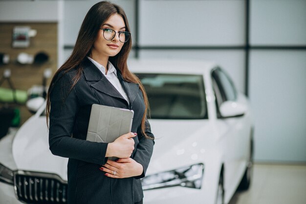 Joven mujer de ventas en carshowroom de pie junto al coche