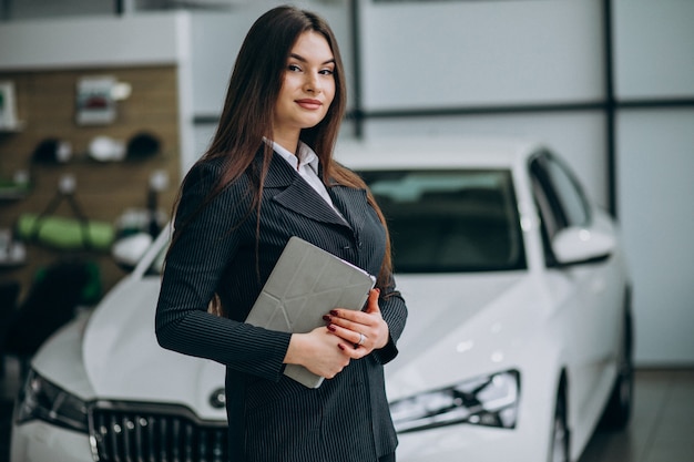 Joven mujer de ventas en carshowroom de pie junto al coche