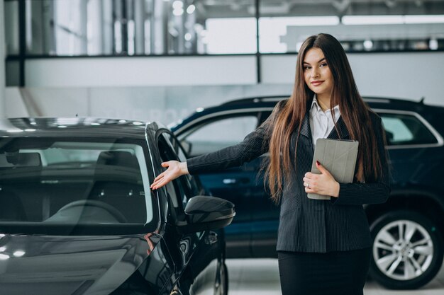 Joven mujer de ventas en carshowroom de pie junto al coche