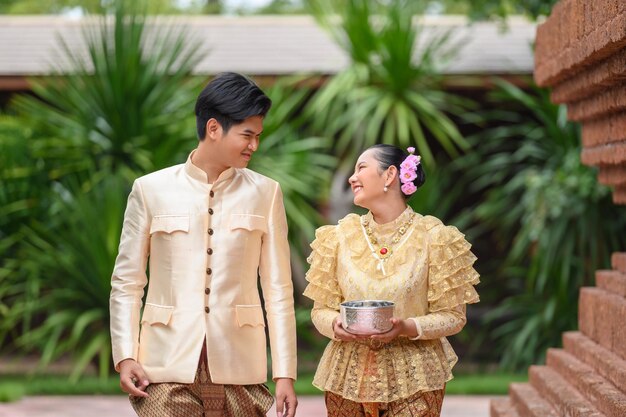 Joven y mujer vestidos con hermosos trajes tailandeses sosteniendo un cuenco de agua en el templo y preservando la buena cultura de los tailandeses durante el festival songkran, día de la familia del año nuevo tailandés en abril