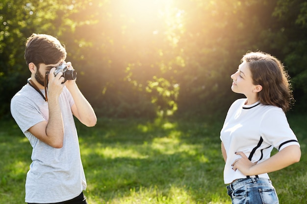 Joven mujer vistiendo camiseta posando en la cámara al fotógrafo. Joven talentoso con cámara retro fotografiando mujer bonita