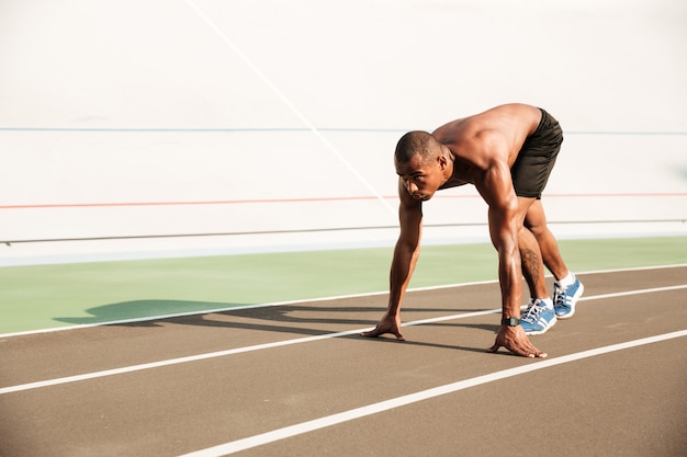 Joven musculoso africano deportista en posición inicial listo para comenzar