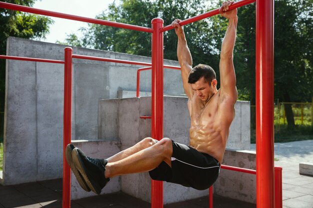 Joven musculoso sin camisa hombre caucásico haciendo abdominales en barra horizontal