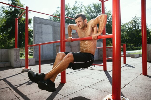 Joven musculoso sin camisa hombre caucásico haciendo dominadas en barra horizontal