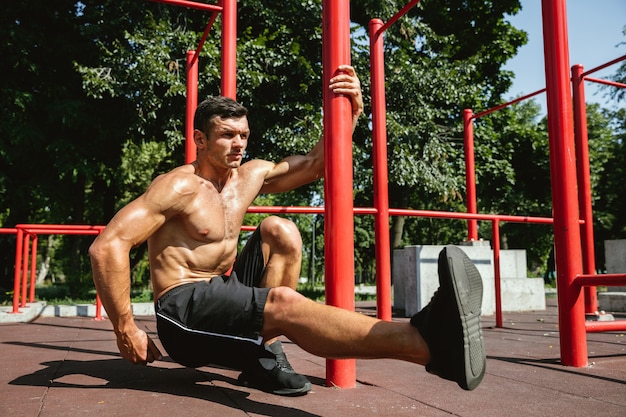 Joven musculoso sin camisa hombre caucásico haciendo sentadillas cerca de la barra horizontal