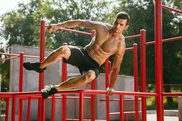 Joven musculoso sin camisa hombre caucásico saltando por encima de la barra horizontal