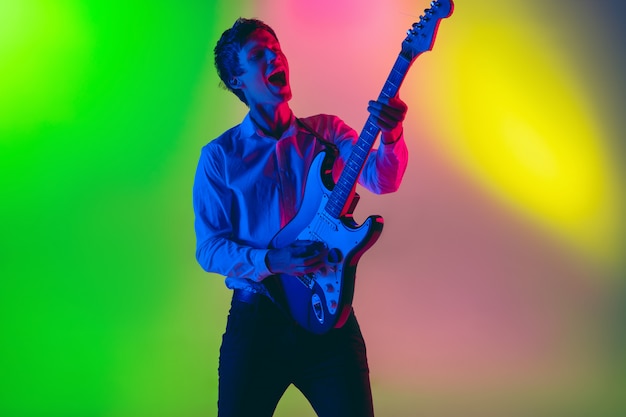 Joven músico caucásico, guitarrista tocando en el espacio degradado en luz de neón. Concepto de música, hobby, festival.