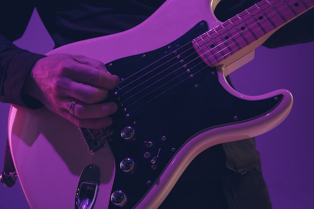 Joven músico caucásico tocando la guitarra en luz de neón en púrpura