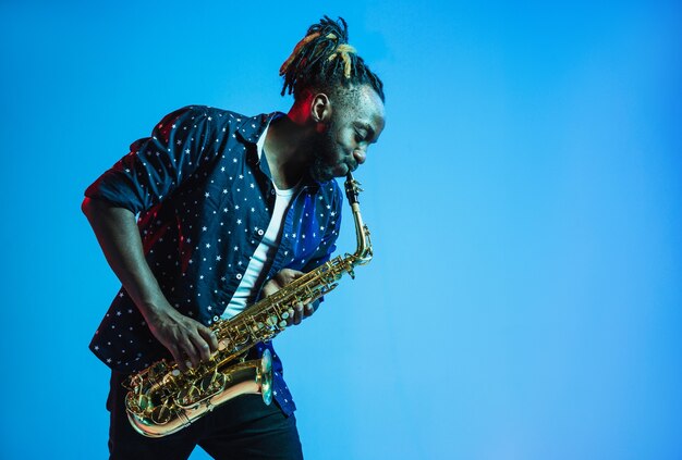 Joven músico de jazz afroamericano tocando el saxofón en azul