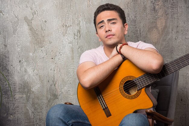 Foto gratuita joven músico sosteniendo la guitarra sobre fondo de mármol