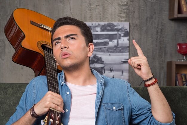 Joven músico sosteniendo una hermosa guitarra y sentado en el sofá. Foto de alta calidad