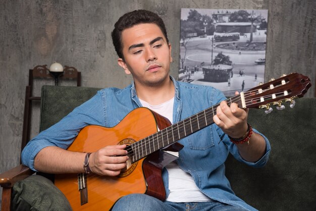 Joven músico tocando la guitarra y sentado en el sofá. Foto de alta calidad