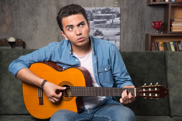 Joven músico tocando la guitarra y sentado en el sofá. Foto de alta calidad