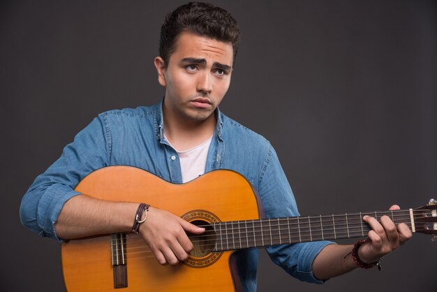 Joven músico tocando la guitarra sobre fondo negro