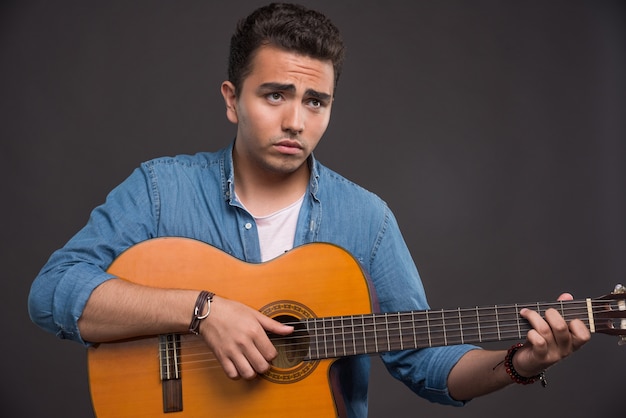 Joven músico tocando la guitarra sobre fondo negro