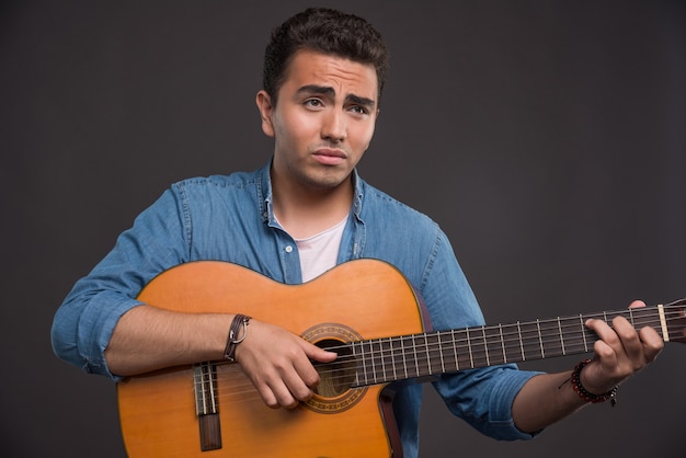 Joven músico tocando la guitarra sobre fondo negro